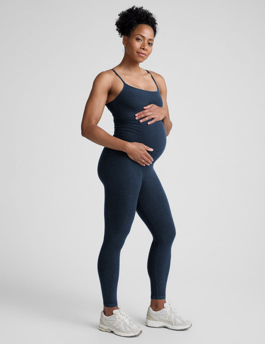 Pregnant woman wearing a navy blue jumpsuit on a light gray background.