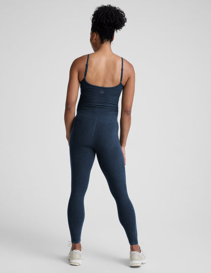 Pregnant woman wearing a navy blue jumpsuit on a light gray background.