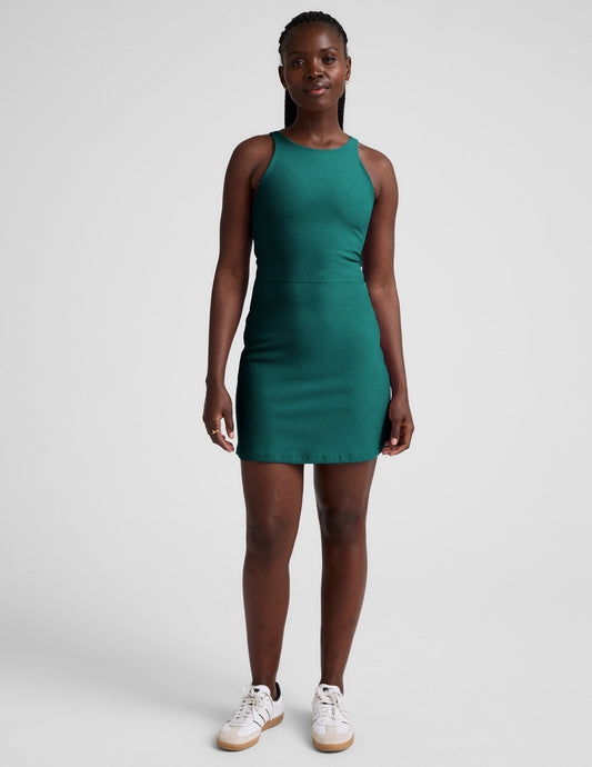 Woman wearing a green high-neck racerback mini dress against a plain background.