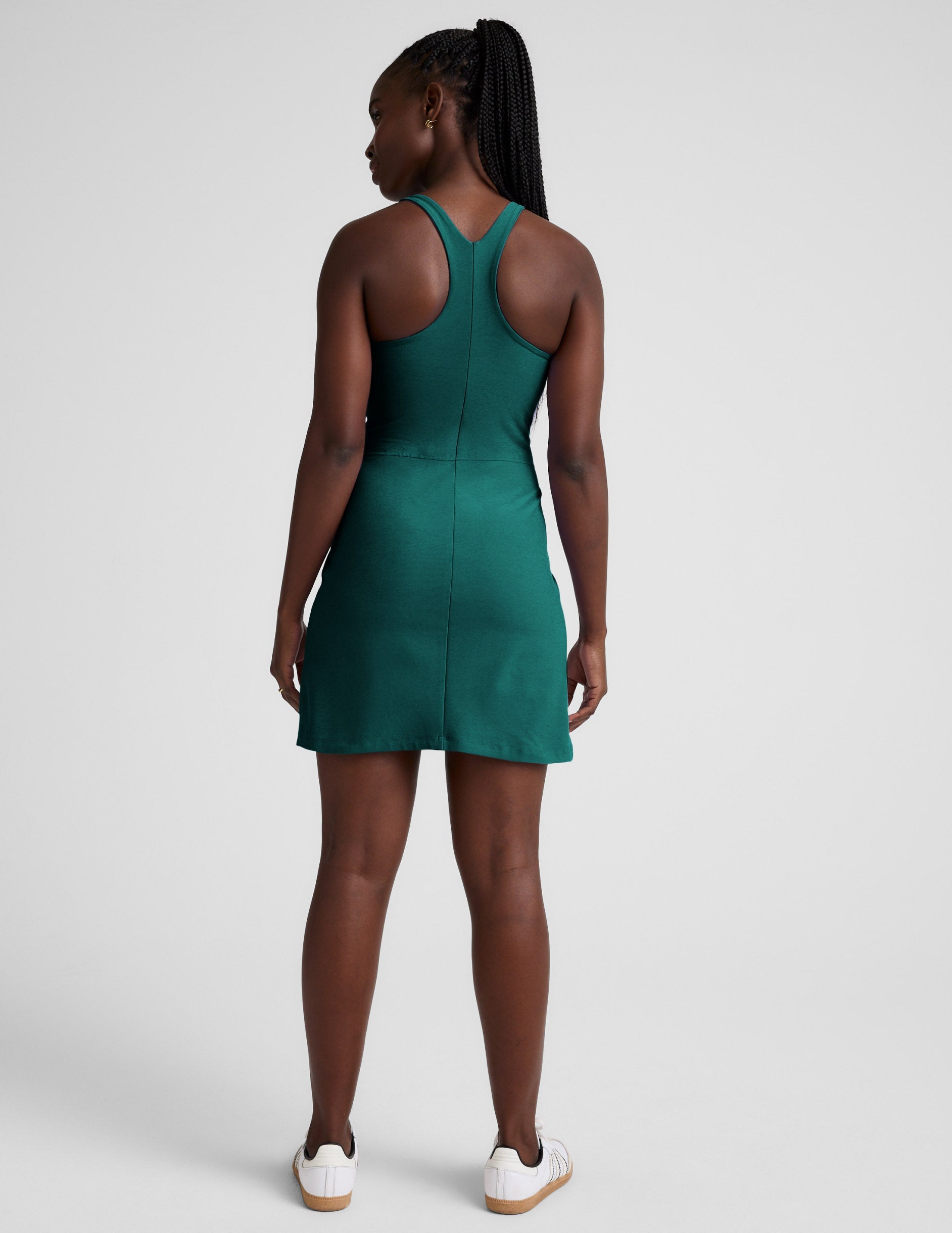 Woman wearing a green high-neck racerback mini dress against a plain background.