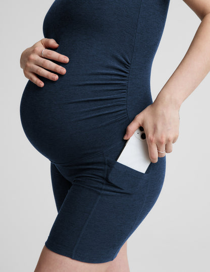 Pregnant woman wearing a navy blue maternity outfit on a light gray background.