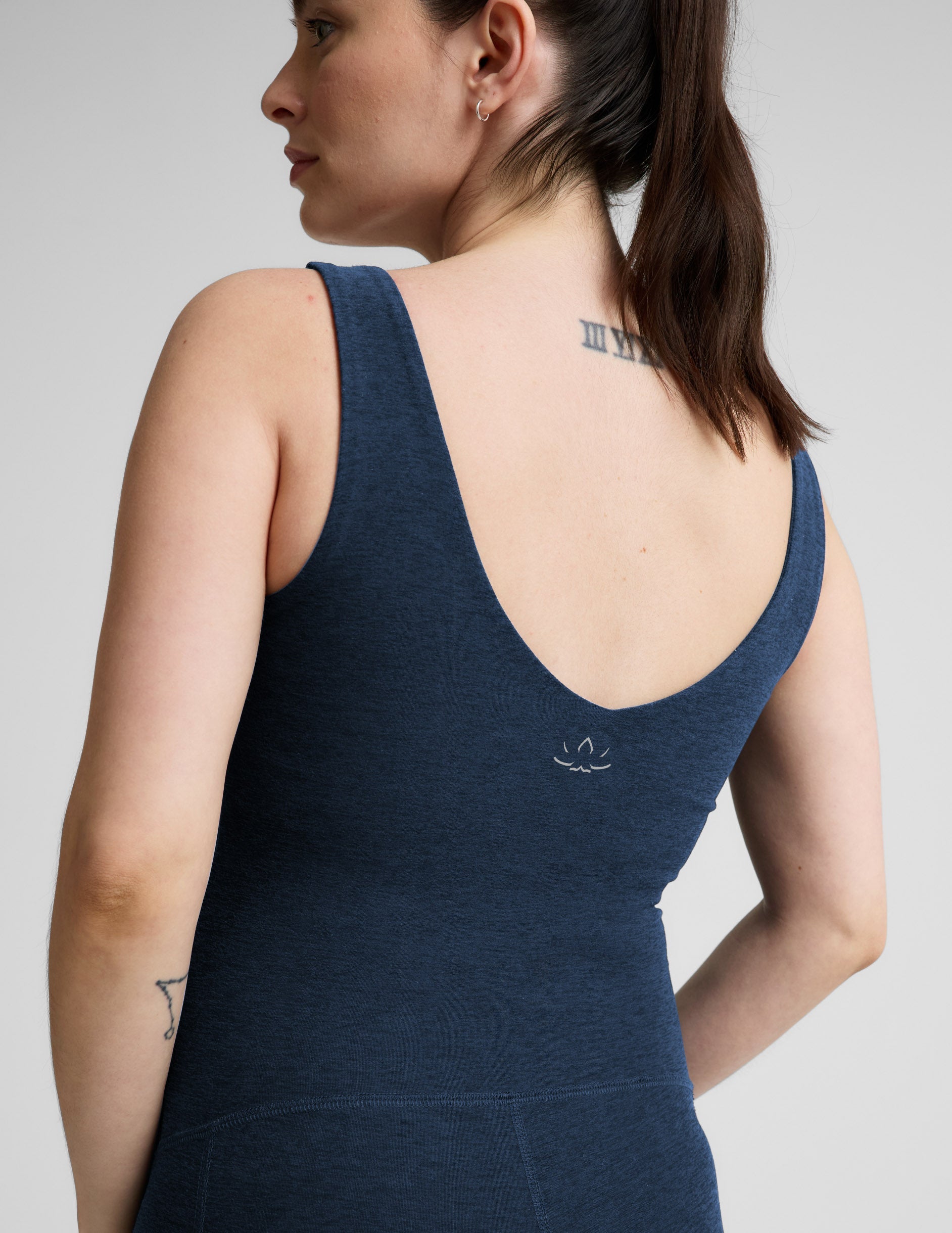 Pregnant woman wearing a navy blue maternity outfit on a light gray background.