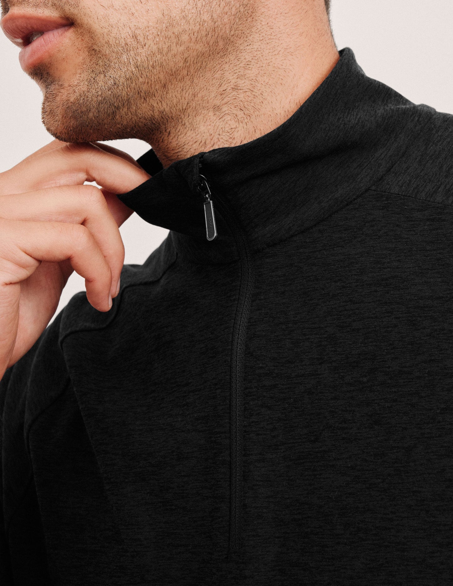 model wearing a black jacket with a zipper, touching the collar against a neutral background.