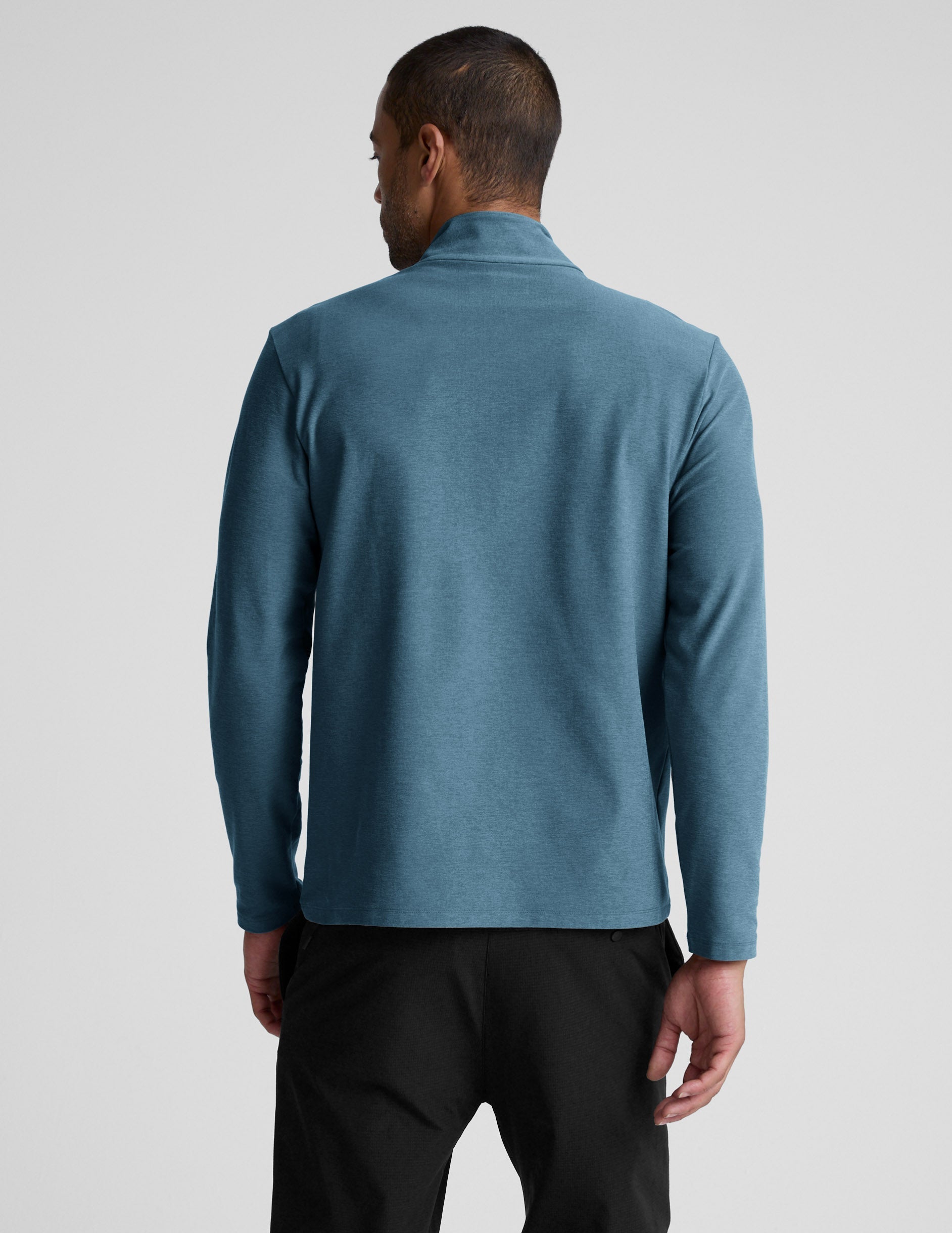Man wearing a blue long-sleeve with a quarter zip and black pants on a light gray background.