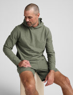 Man wearing a green hoodie and shorts sitting on a white surface.