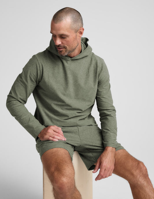 Man wearing a green hoodie and shorts sitting on a white surface.