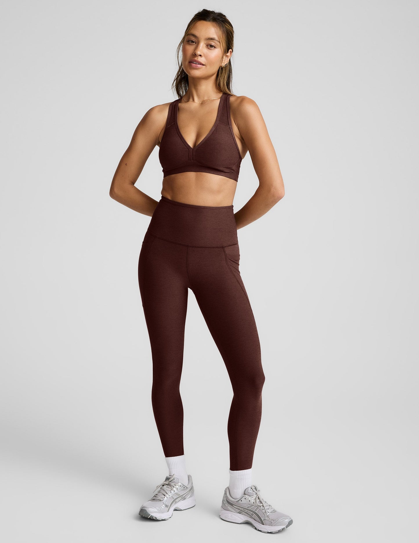 Woman wearing a brown sports bra and leggings against a light gray background.