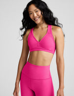 Woman wearing a pink sports bra and leggings on a gray background.