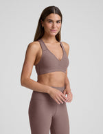 Woman wearing a brown sports bra and leggings on a light gray background.