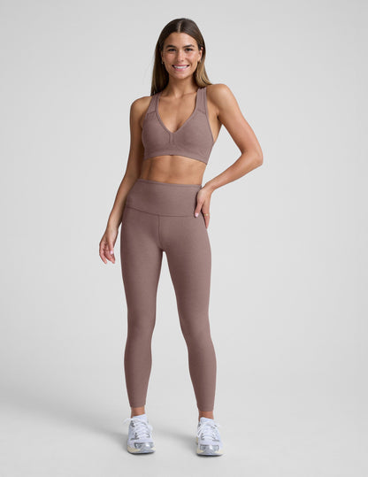 Woman wearing a brown sports bra and leggings on a light gray background.