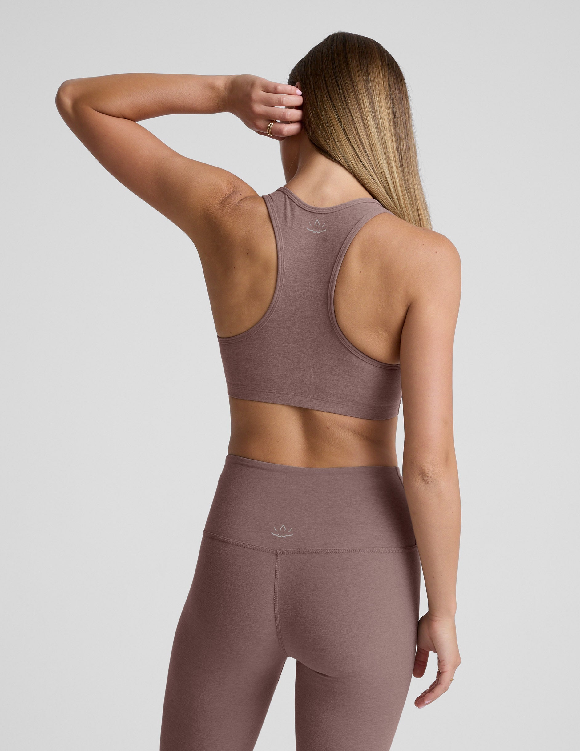 Woman wearing a brown sports bra and leggings on a light gray background.