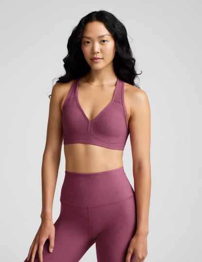Woman wearing a purple bra and leggings against a plain background.