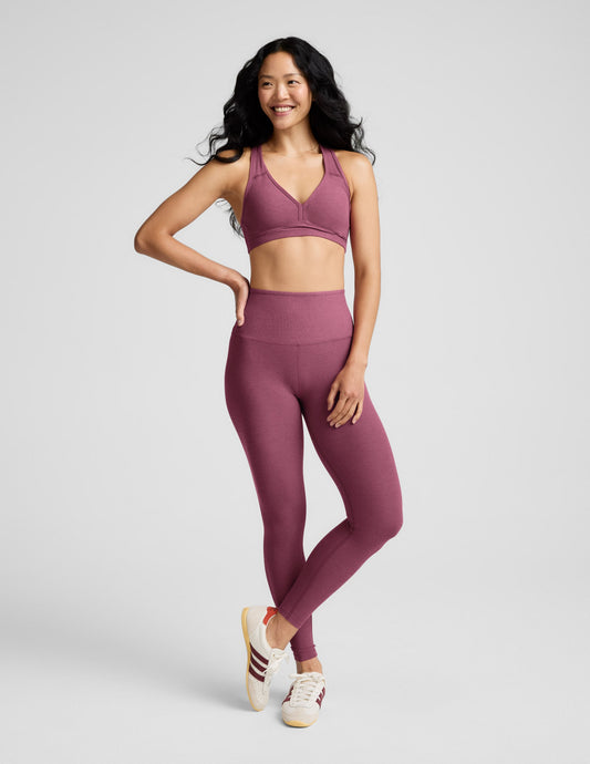 Woman wearing a purple bra and leggings against a plain background.