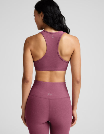 Woman wearing a purple bra and leggings against a plain background.