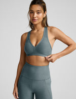 Woman wearing a gray sports bra and leggings on a light gray background.