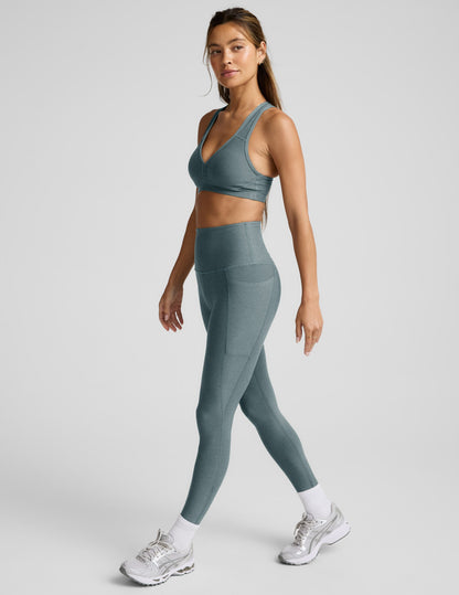 Woman wearing a gray sports bra and leggings on a light gray background.