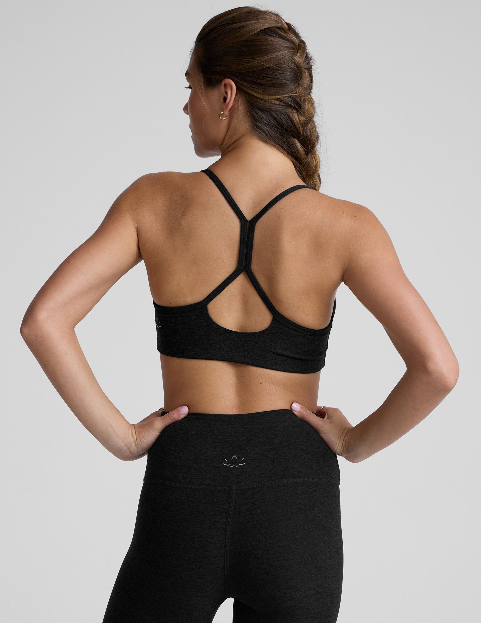 woman wearing a black slim racerback bra and leggings on a plain background.