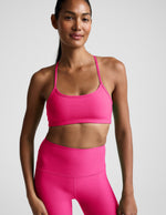 Woman wearing a bright pink sports bra and leggings on a light gray background.