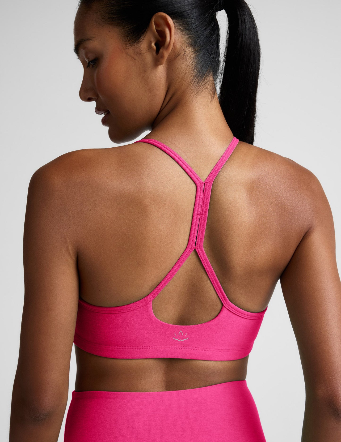 Woman wearing a bright pink sports bra and leggings on a light gray background.