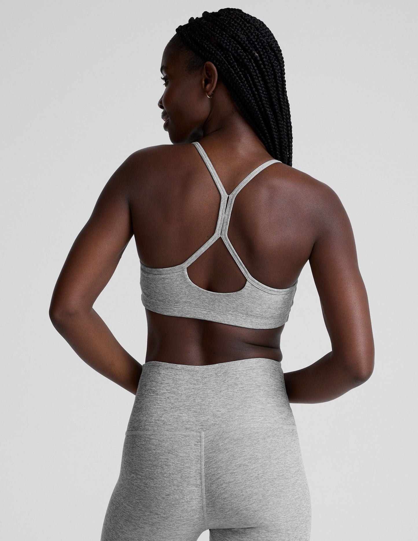 model is wearing a gray racerback bra with slim spaghetti straps and leggings against a plain background.