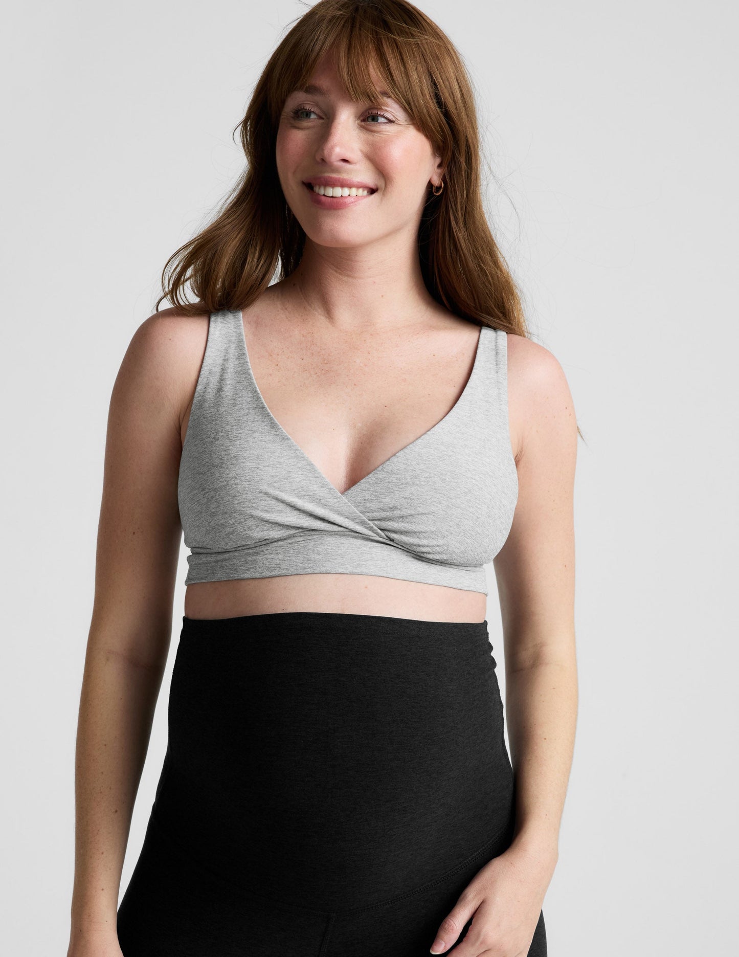Woman wearing a gray nursing bra and black maternity leggings against a plain background.