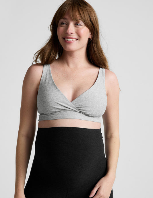 Woman wearing a gray nursing bra and black maternity leggings against a plain background.
