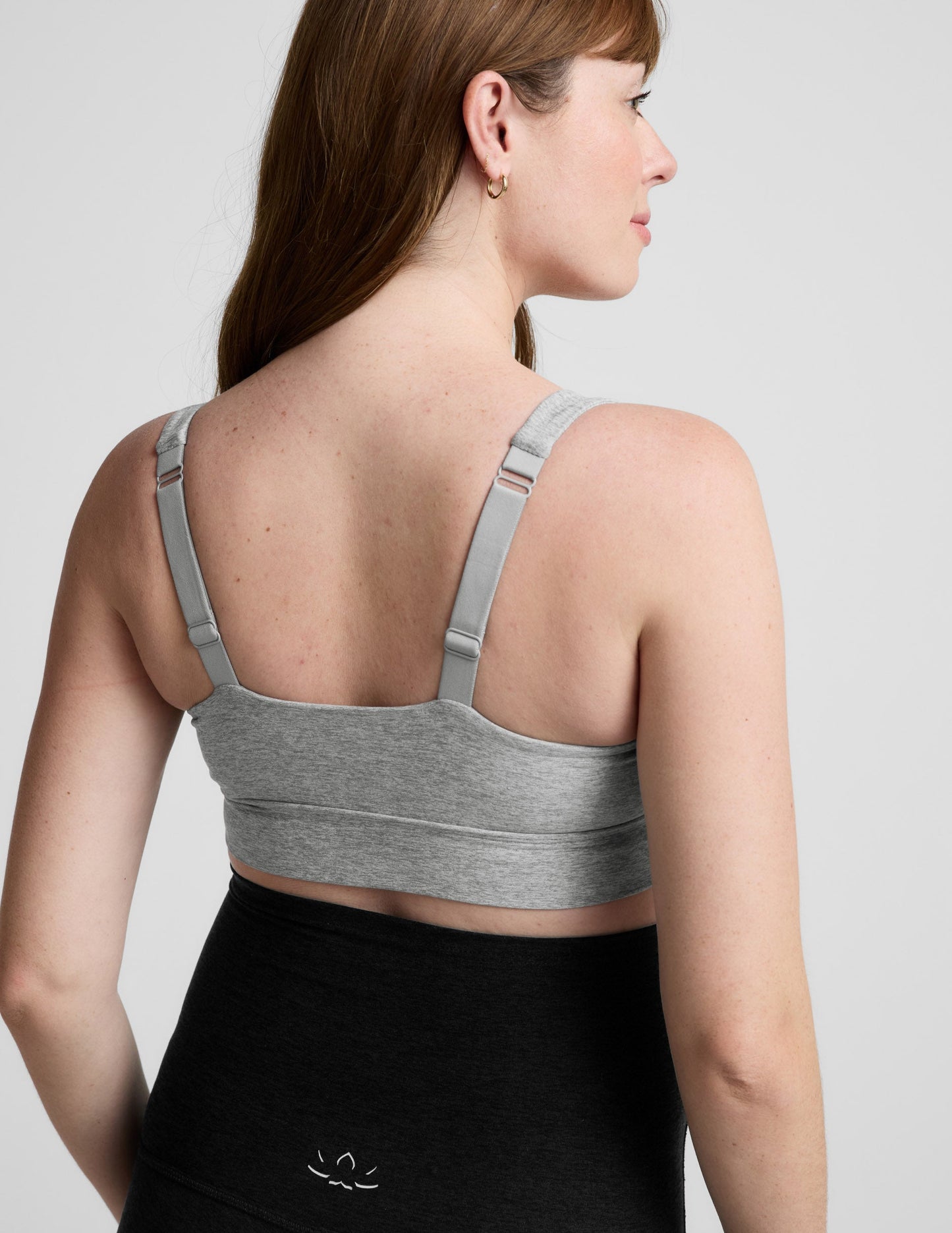 Woman wearing a gray nursing bra and black maternity leggings against a plain background.