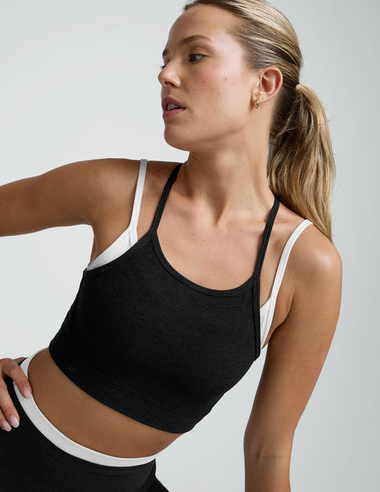Woman wearing a black and white layered racerback sports bra and leggings on a plain background.