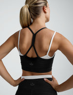 Person wearing a black sports bra with criss-cross straps over a white sports bra.