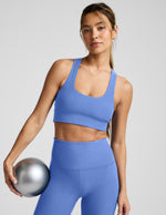Woman wearing a blue sports bra and leggings holding a silver ball against a light gray background.