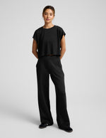 Person wearing a black cropped tee and pants on a light gray background.