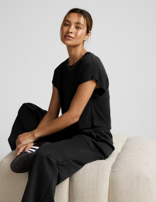 Person wearing a black cropped tee and pants on a light gray background.