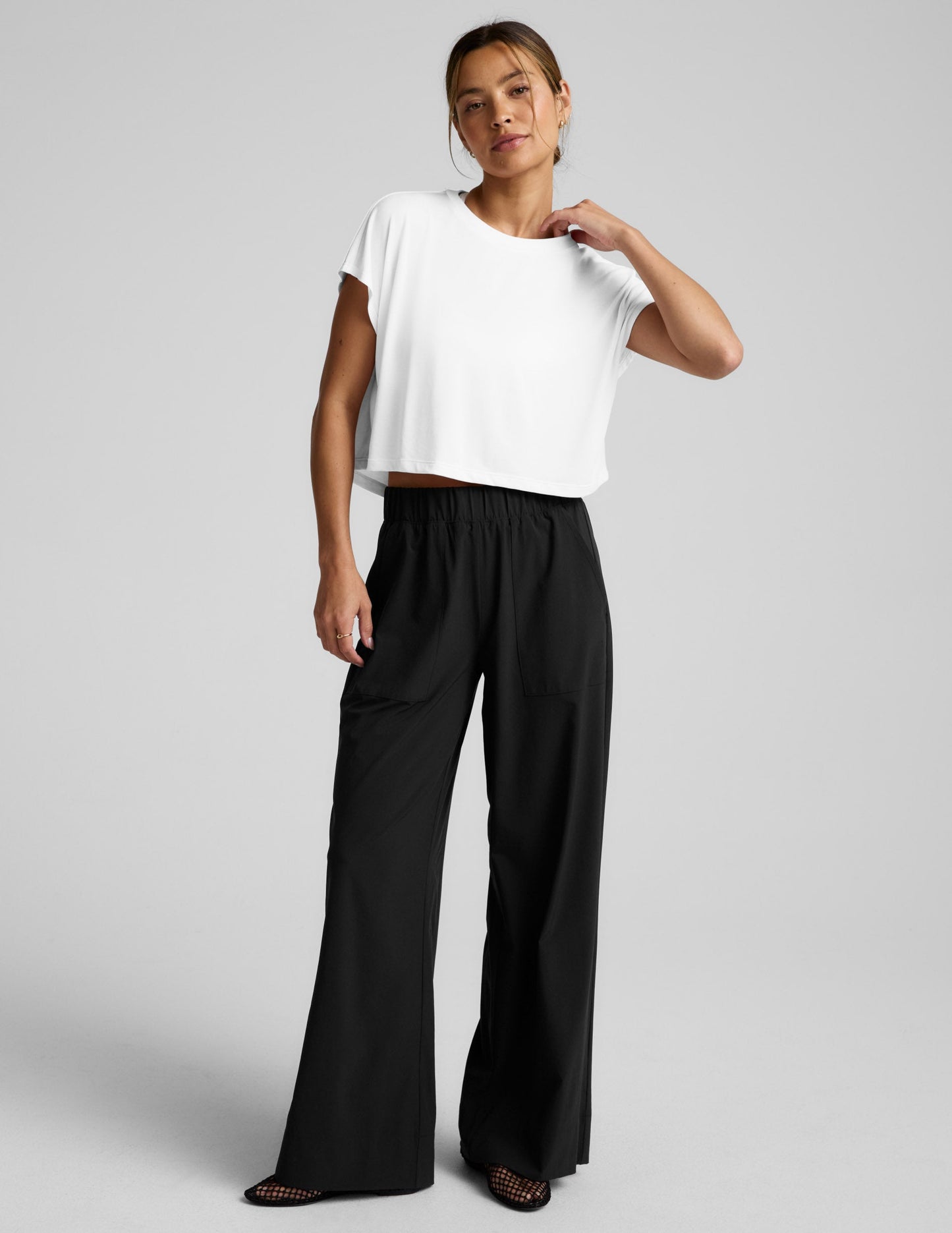 Woman wearing a white top and black pants on a gray background.