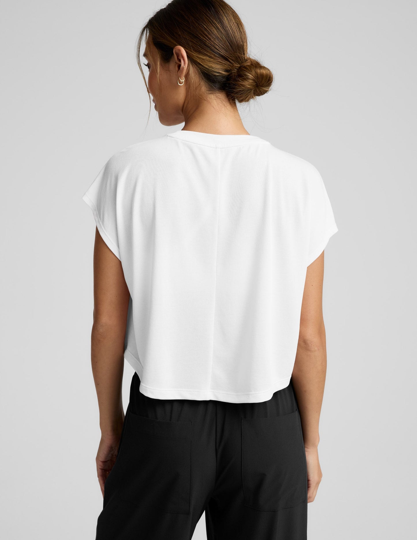 Woman wearing a white top and black pants on a gray background.