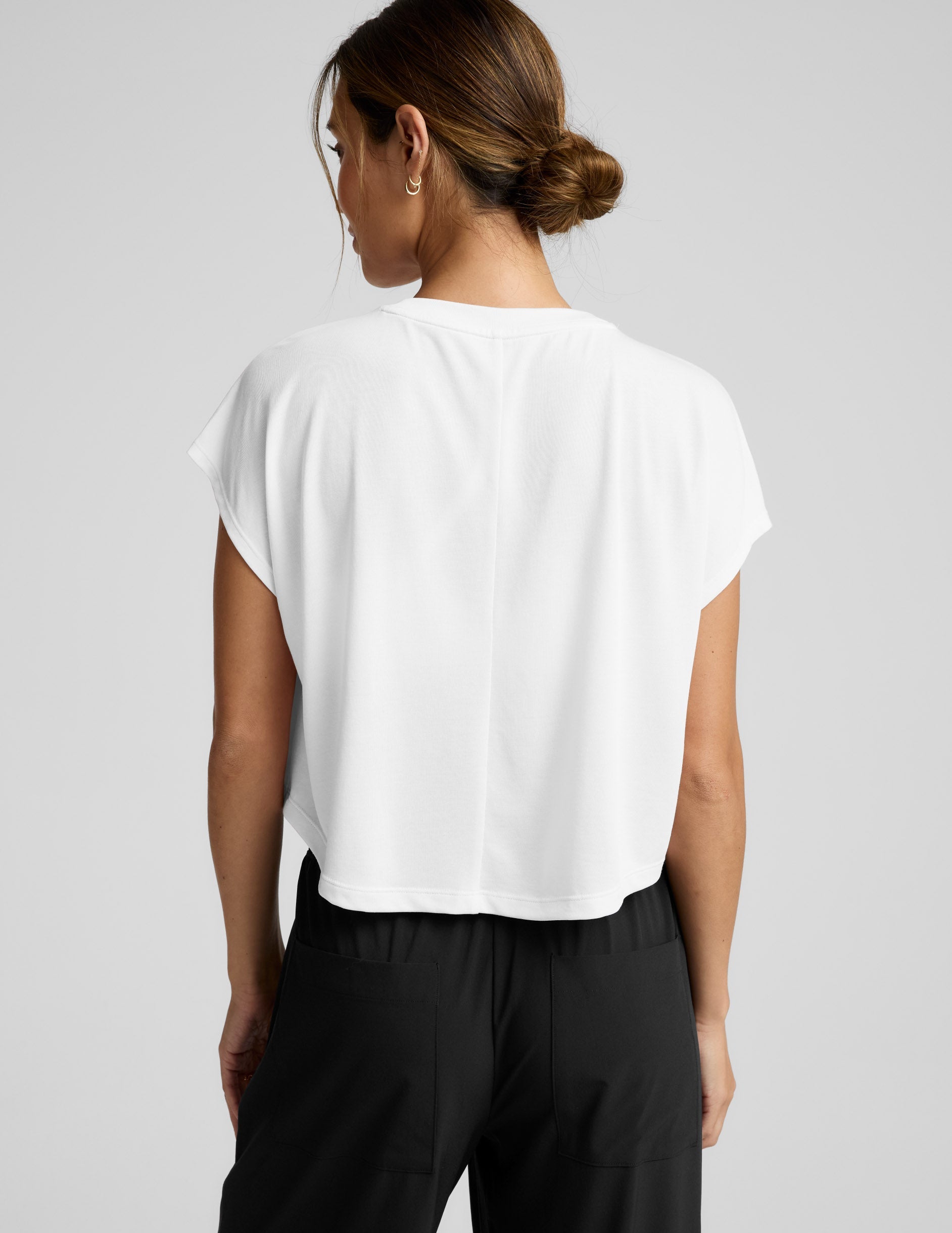 Woman wearing a white top and black pants on a gray background.
