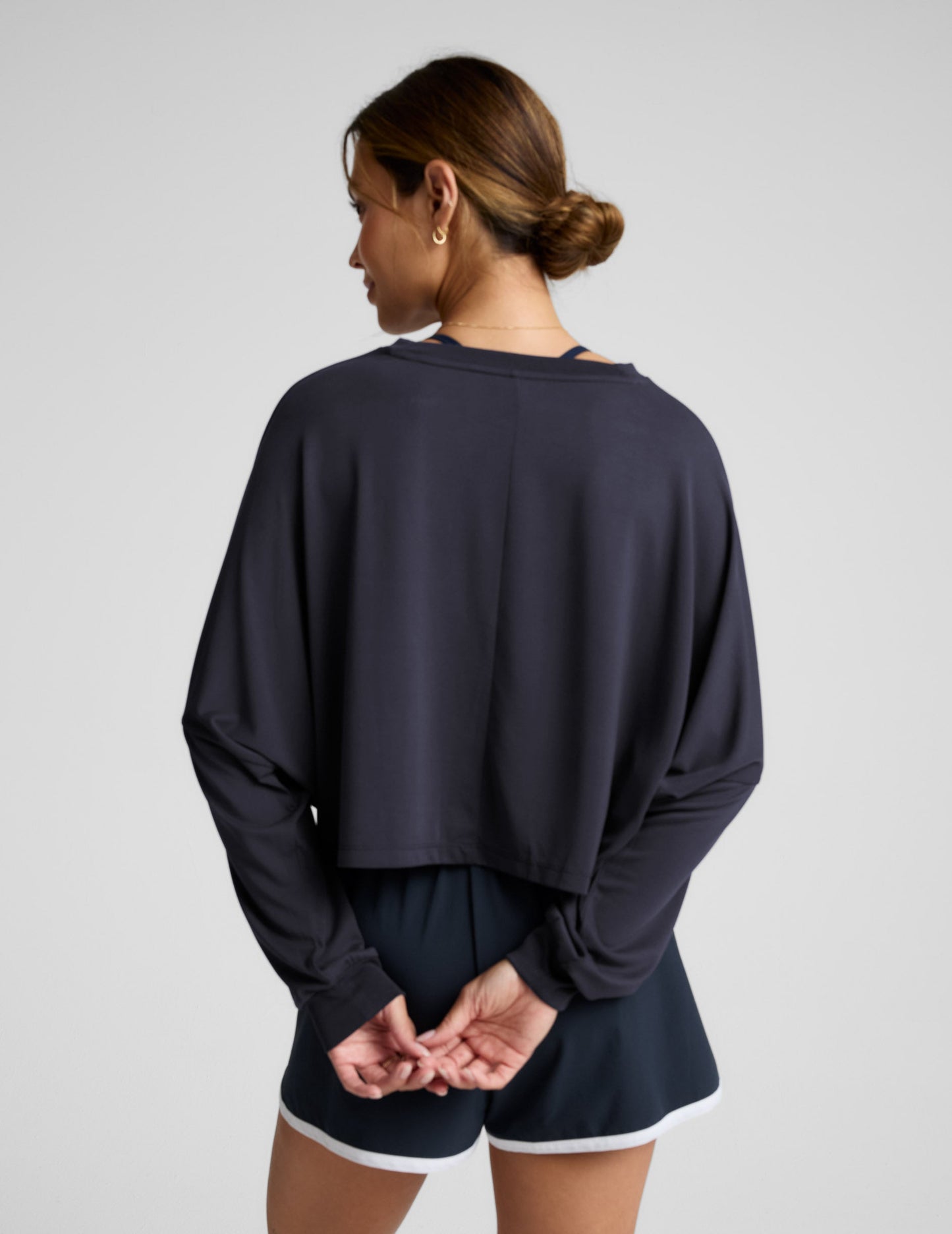 Woman wearing a blue long-sleeve top and blue shorts with white drawstrings on a gray background.