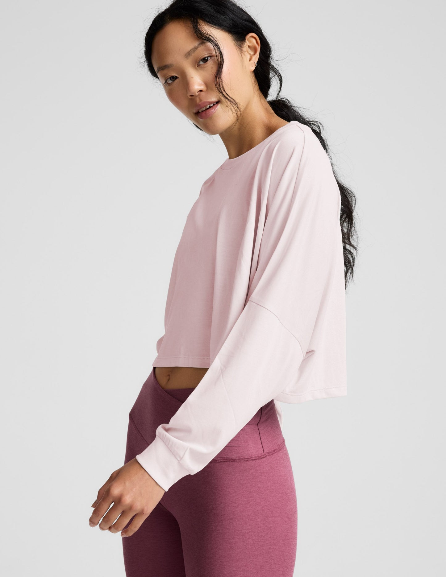 Woman wearing a pink long-sleeve top and mauve leggings indoors.