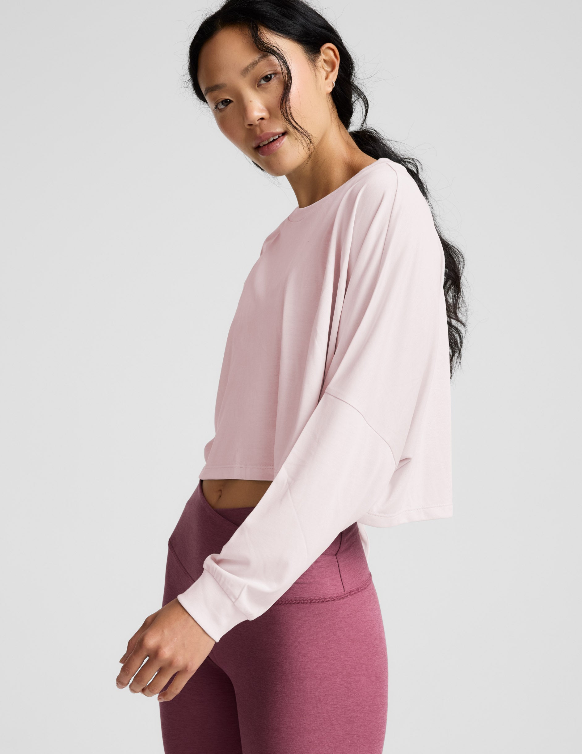Woman wearing a pink long-sleeve top and mauve leggings indoors.