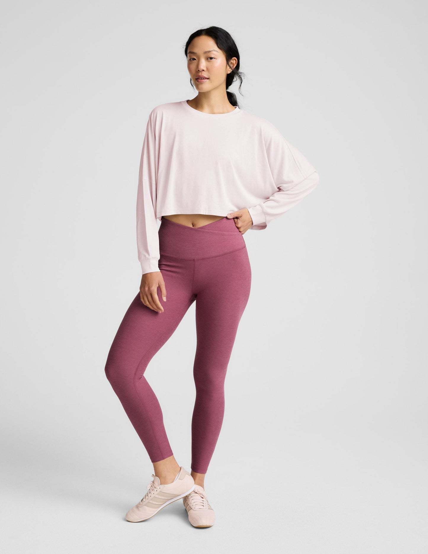 Woman wearing a pink long-sleeve top and mauve leggings indoors.