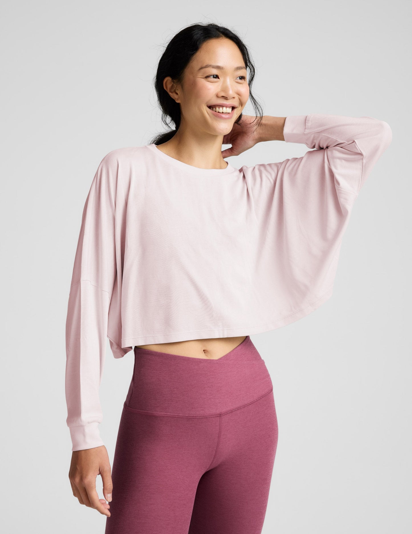 Woman wearing a pink long-sleeve top and mauve leggings indoors.