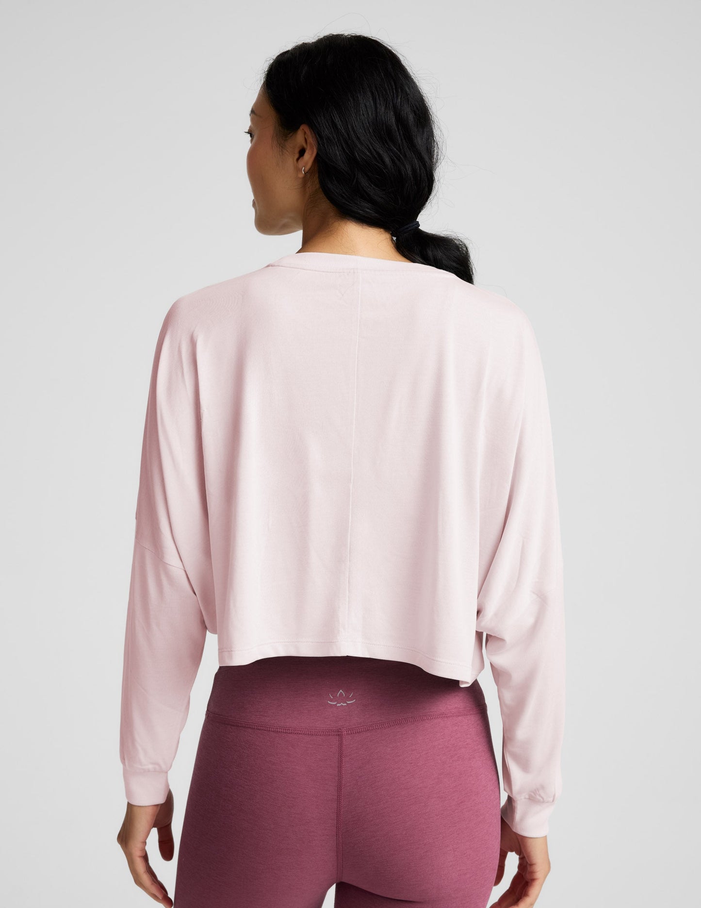 Woman wearing a pink long-sleeve top and mauve leggings indoors.