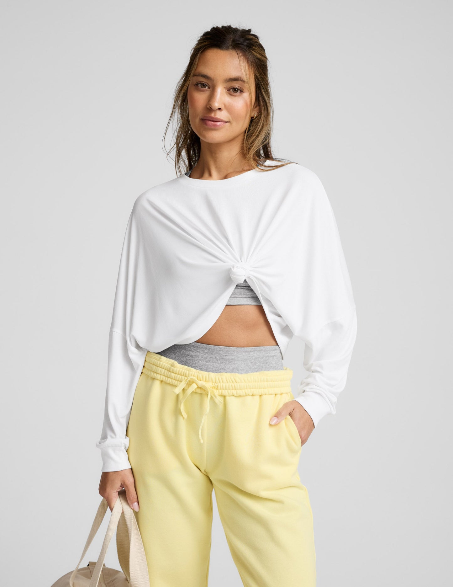 Woman wearing a white long-sleeve top and yellow pants on a gray background.