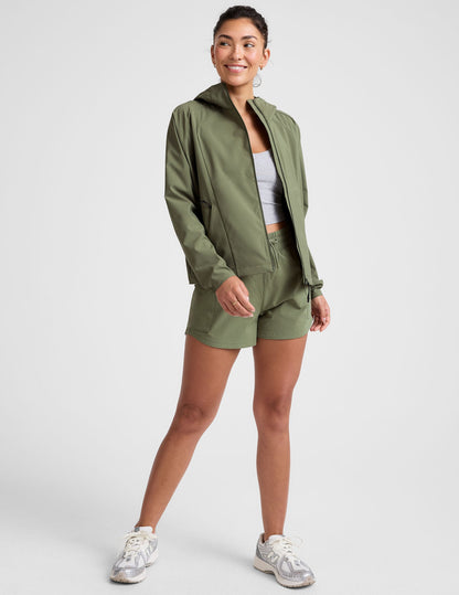 model is wearing an olive green zip-up jacket with side pockets and a hood on a white background.