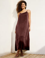 Woman wearing a brown cupro maxi dress leaning against a wall.