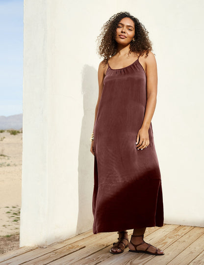 Woman wearing a brown cupro maxi dress leaning against a wall.