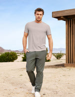 Man in casual clothing standing in a desert-like setting with mountains in the background.