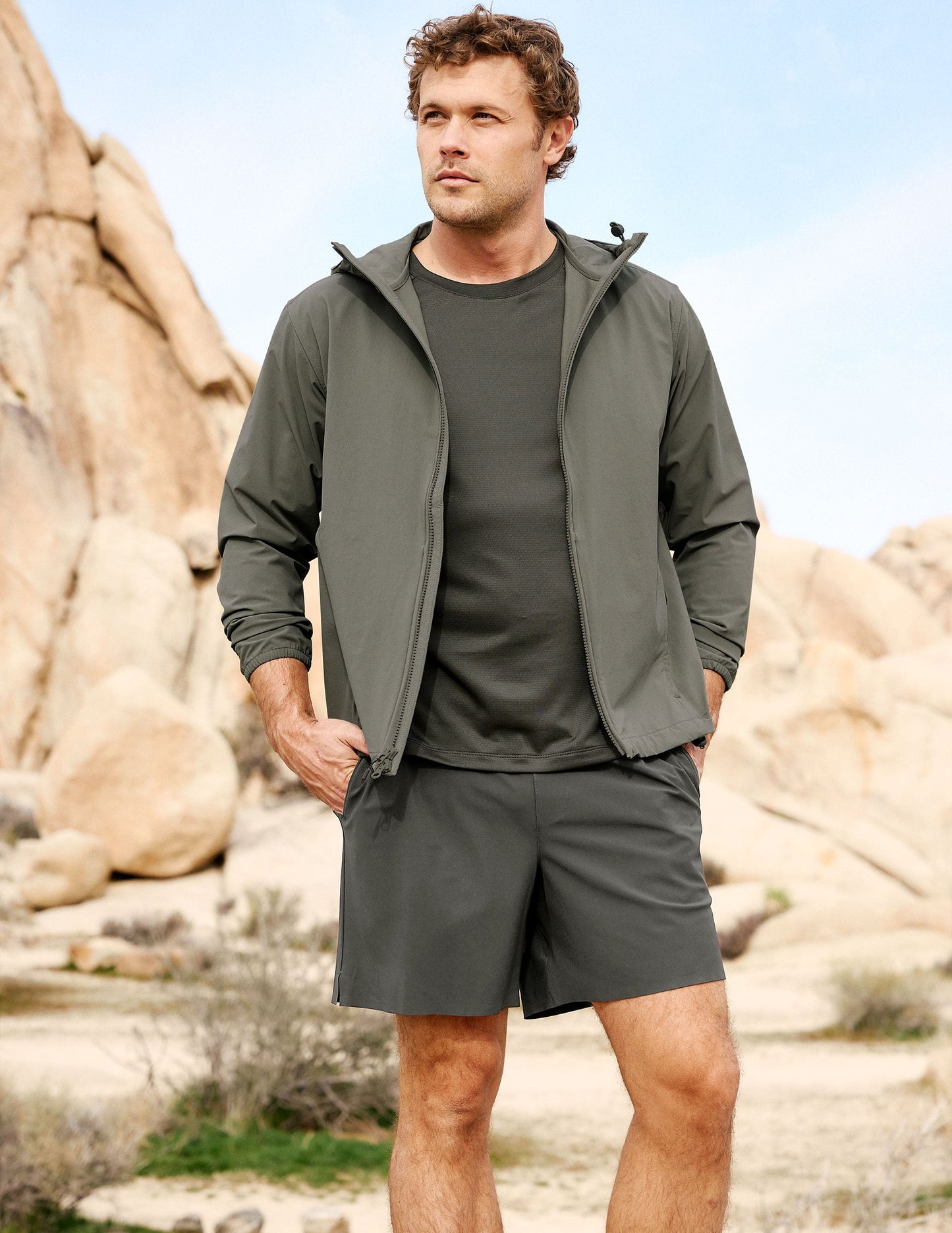 Man wearing a gray jacket and shorts standing in a desert landscape.
