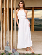 Woman in a white dress standing in front of wooden panels with desert landscape in the background.