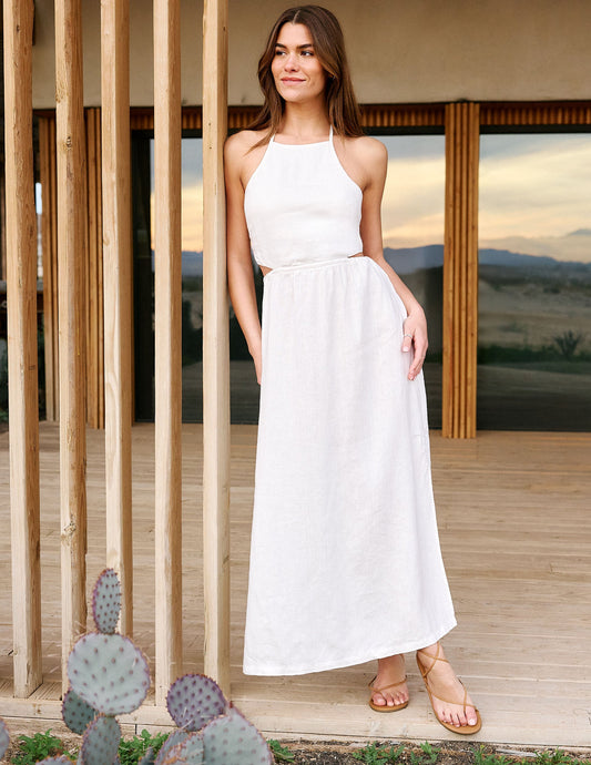 Woman in a white dress standing in front of wooden panels with desert landscape in the background.