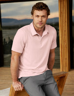 Man wearing a pink polo top and gray pants sitting in front of a house.